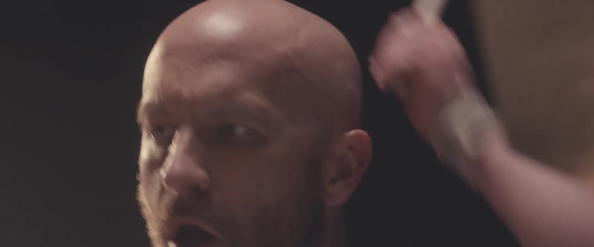 Bald muscular man playing drums on a stage under a spotlight