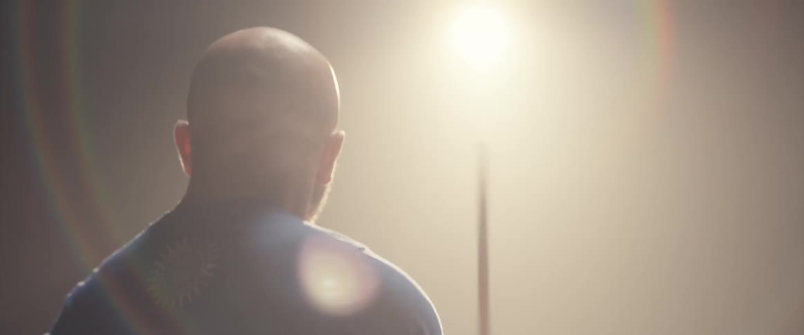 A light shines and glares on a man playing the drums in a dark space