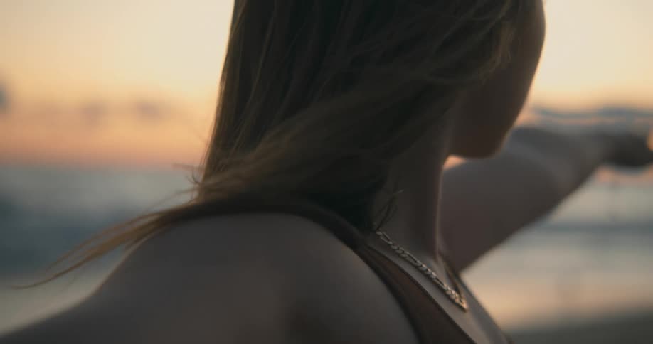 Young blonde woman holding a yoga pose on the sand beach at sunset next to the ocean