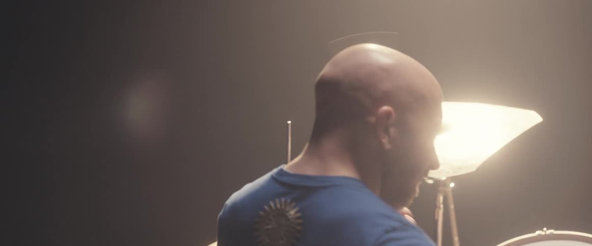 A man is holding drumsticks and playing the drums as a light shines above him