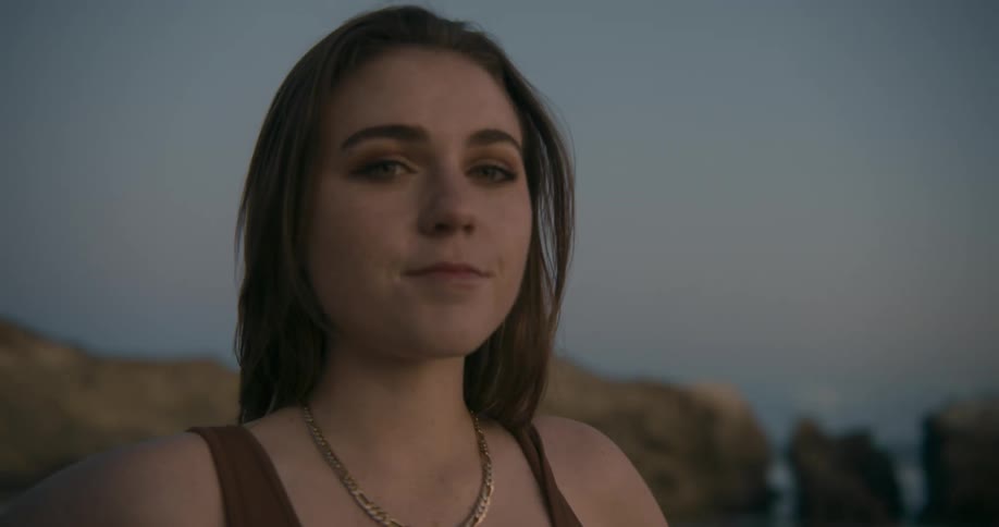 Young woman standing on the sand beach at sunset next to the ocean looks at the camera