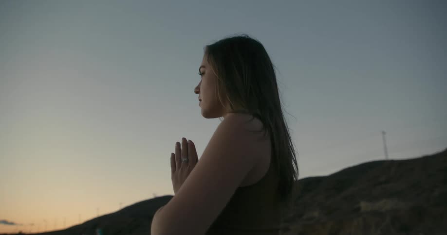A young woman faces the ocean while practicing yoga on a beach at sunset