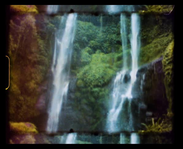A pair of waterfalls down a tall cliff covered in vegetation in the wilderness during the day