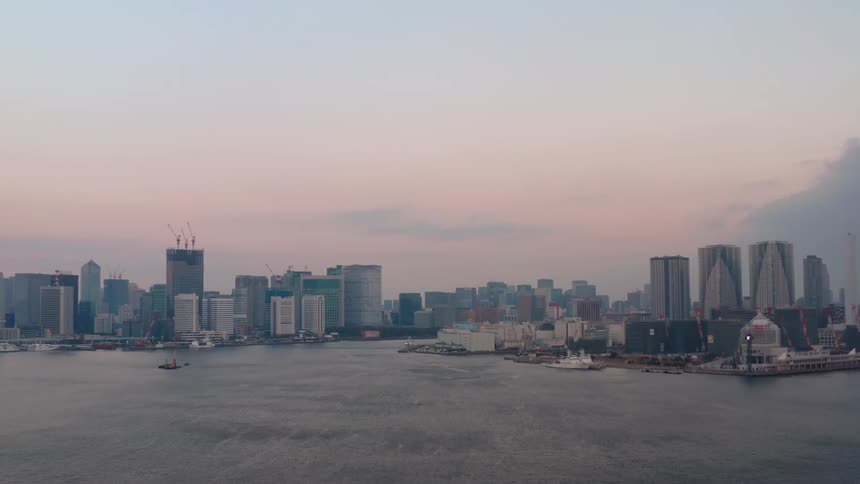 Construction cranes work on buildings near water front under a red sky