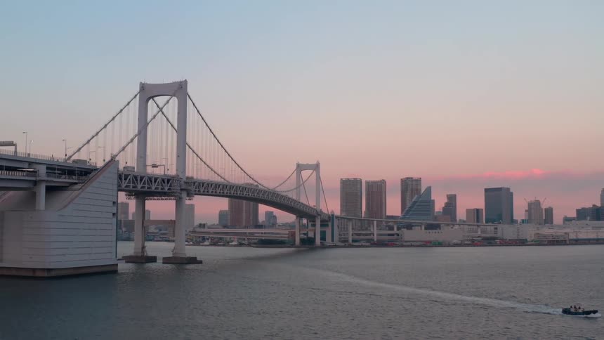 Aerial view of a suspension bridge over a river in front of the city skyline at evening