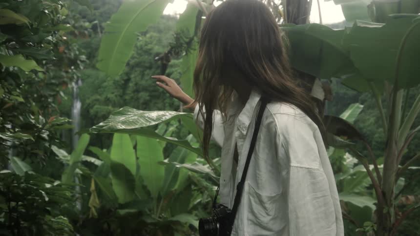 Young woman leisurely walking along tropical trees at evening