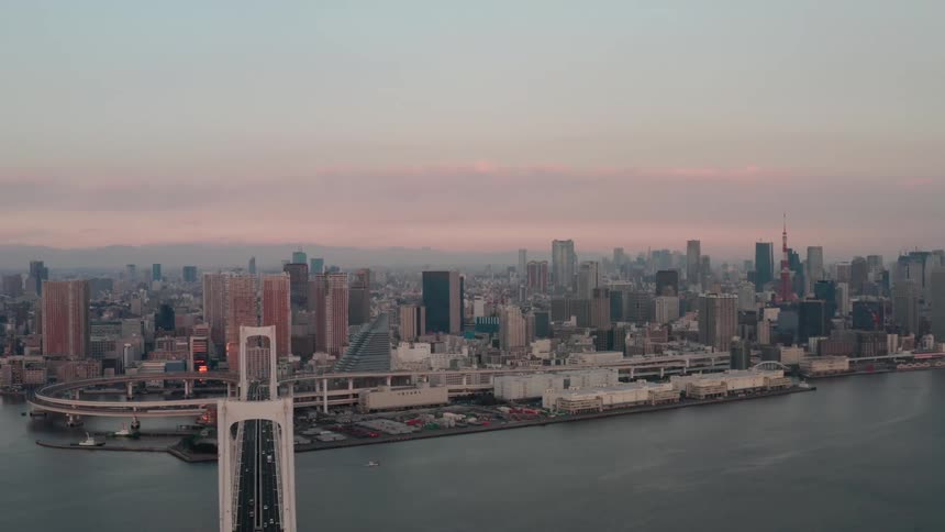 Traffic crosses over water on bridge toward downtown under red sky