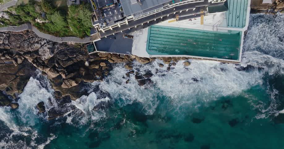 Aerial view of people swimming on a pool inside a building over a cliff in the coast
