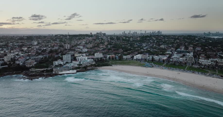 Aerial view of a beach in front of a neighborhood close to the city skyline at evening
