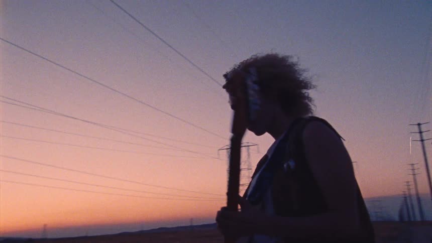 Female guitarist plays instrument while standing on country road as afterglow turns sky red