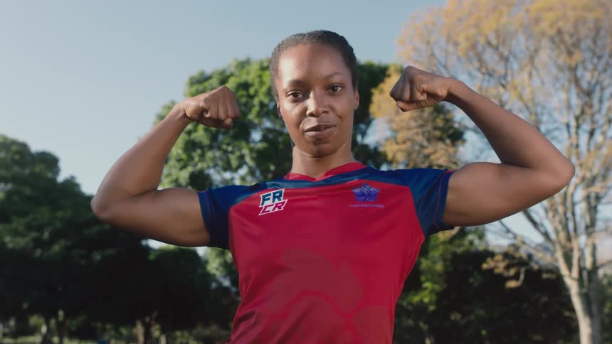 Young woman stands outdoors showing her muscles looking at the camera