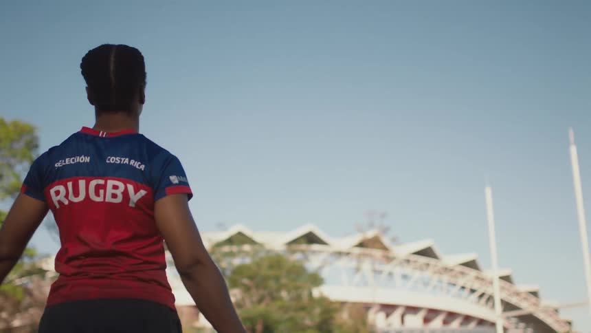 A female rugby player stretches her arms while standing outdoors during the day