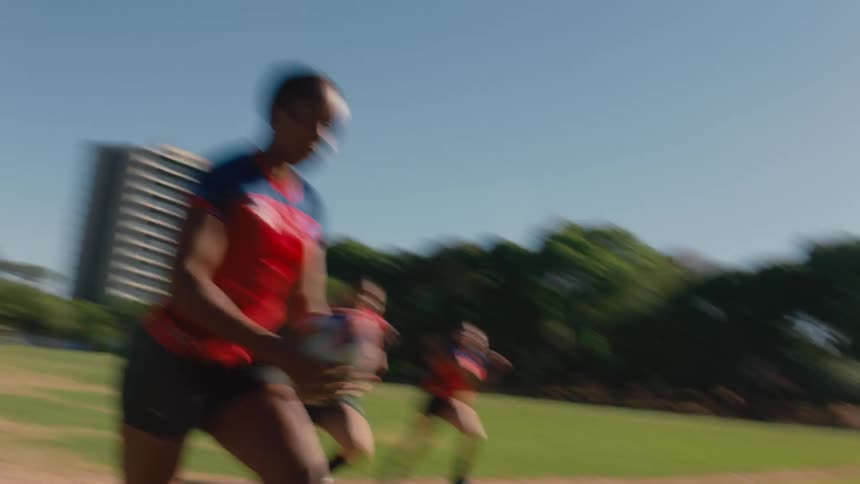 A woman catches the ball and runs down the grass field with her rugby teammates