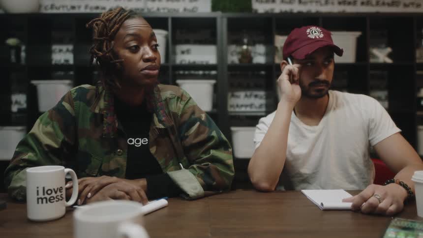 A man and woman sit at a conference table and listen to a workplace discussion