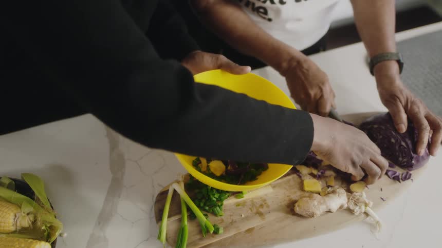 Woman cuts red cabbage and puts in yellow plastic bowl in the kitchen