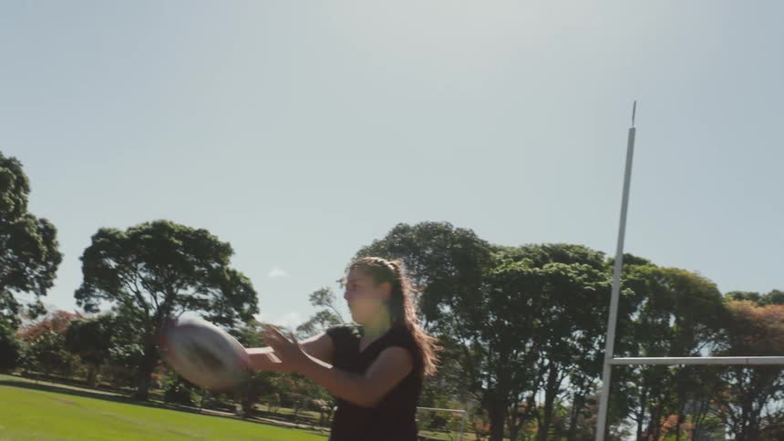 A group of women practice passing a rugby ball on athletics field during the day