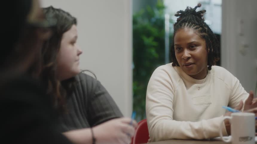 A woman talks to the people sitting with her around a table indoors during the day