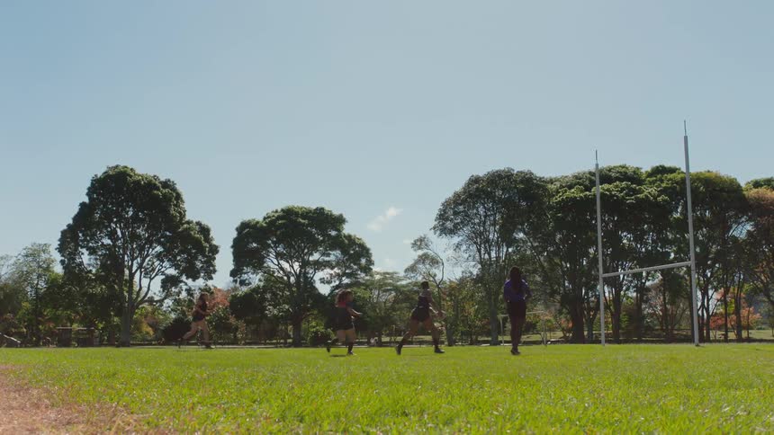 Women play with a football on field next to goal post