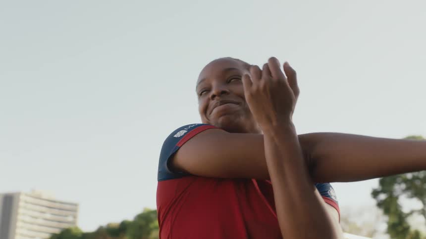 A female athlete performs arm stretches while standing outdoors during the day