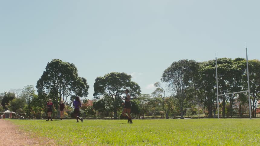 A group of people run on a football field and one person passes the ball to another