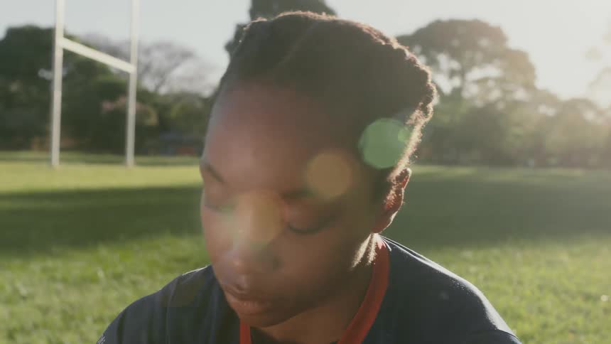 Close up of the face of a young woman sitting over the grass on a football field at morning