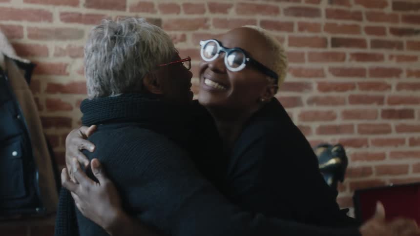 Woman helps elderly woman stand then they hug and talk while smiling
