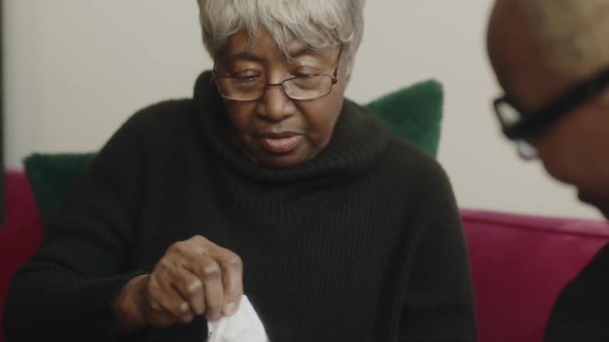 A woman helps her mom open a gift container pulling out a tee shirt with an empowering message