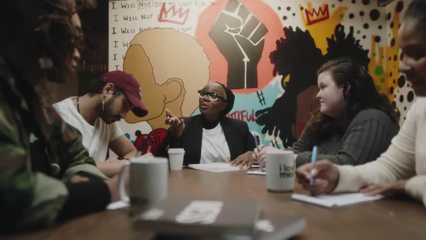 People meet a table near wall mural taking notes while they talk