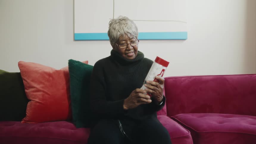 A woman sitting on a couch holding a gift canister looks up and smiles