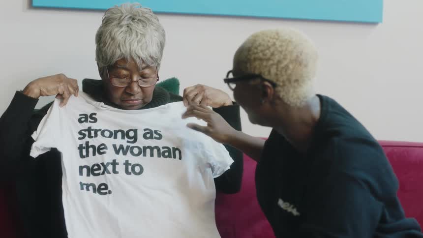 Woman gives t shirt with text on it to elderly woman and they both smile