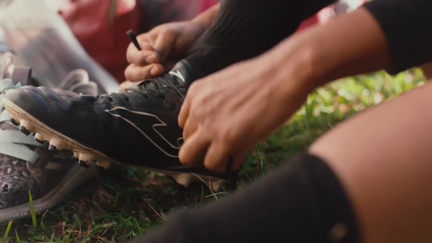 A person sitting in a field ties the shoelaces on their running shoes