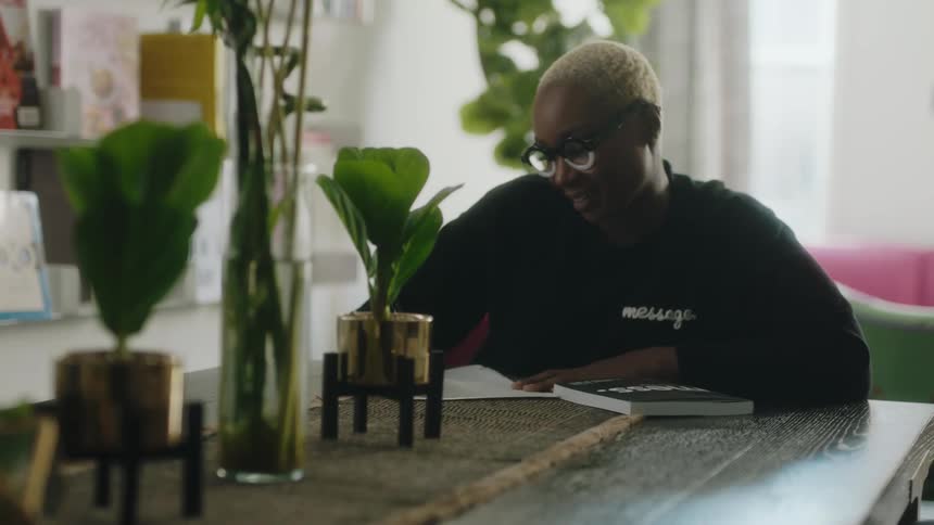 Woman wearing eyeglasses sits at wooden table writing