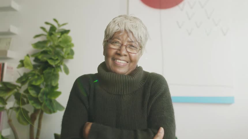 An elderly woman smiles into the camera while sitting indoors
