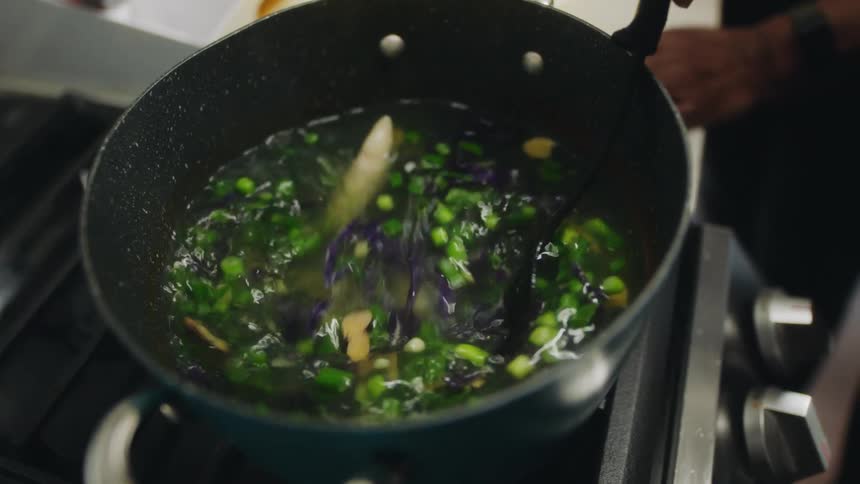 A person uses a stirring spoon to stir the contents of a pot on an oven