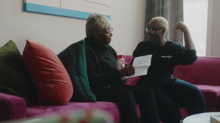Younger woman smiles while talking to elderly woman as they both look at piece of paper