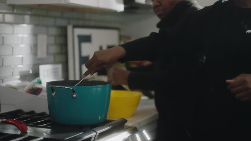 Younger woman smiles while cooking on stove with elderly woman