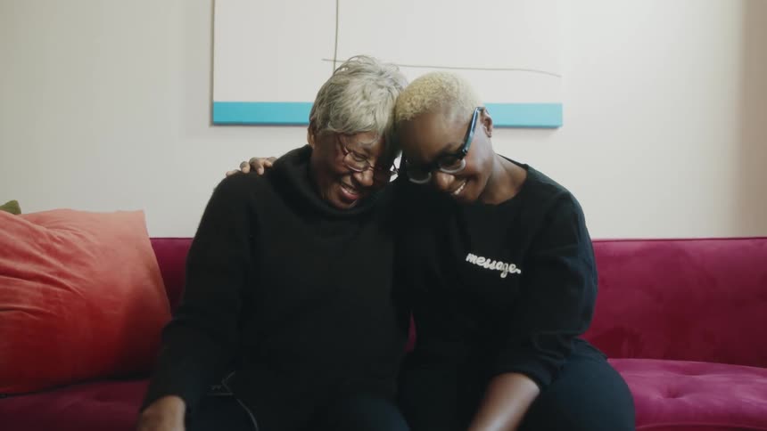 Happy mother and daughter sitting on a couch at home hugging each other