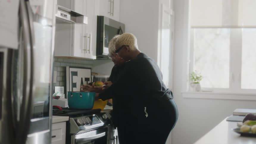 A pair of women cook together in a home kitchen during the day