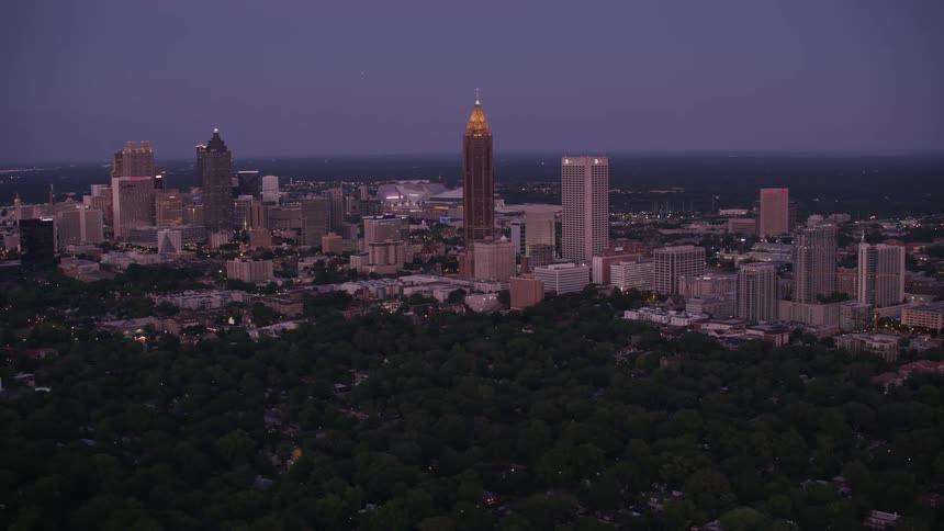 The top of a skyscraper glows orange as it looms over a forest next to downtown