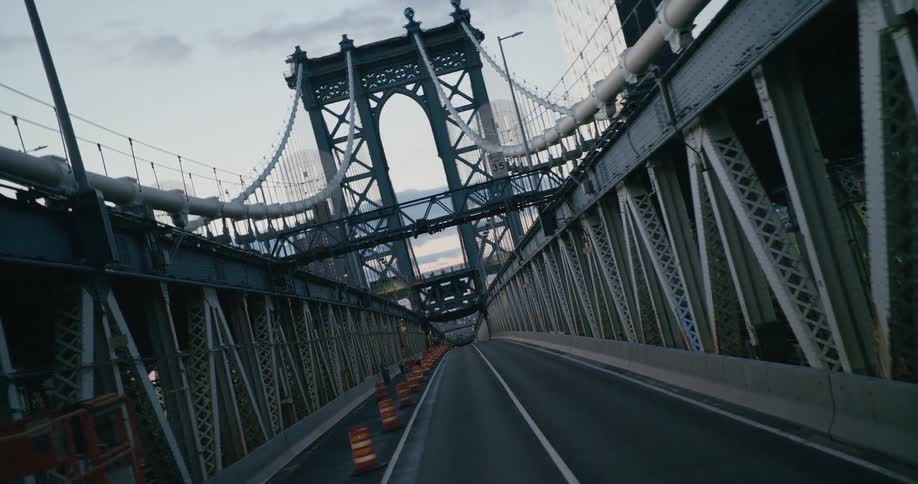 Orange construction barrels line the space between and below a suspension bridge