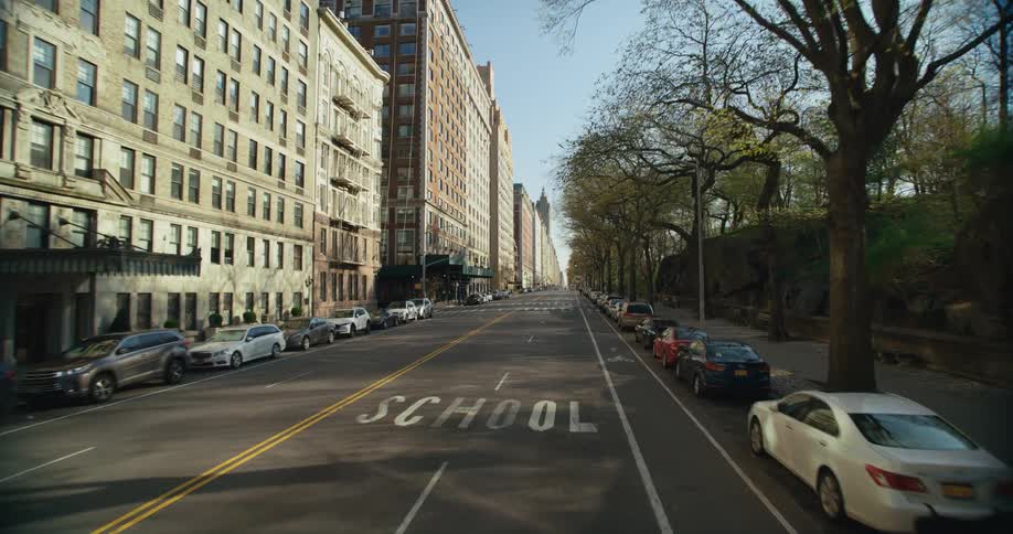Parked vehicles sit on sides of a street passing between apartment buildings and a raised stone area