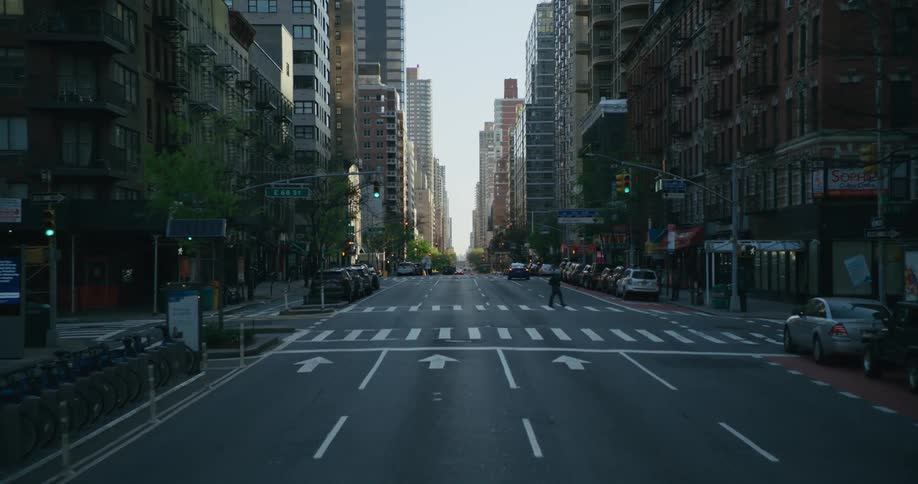 A pedestrian is crossing a downtown street lined with tall buildings and automobiles