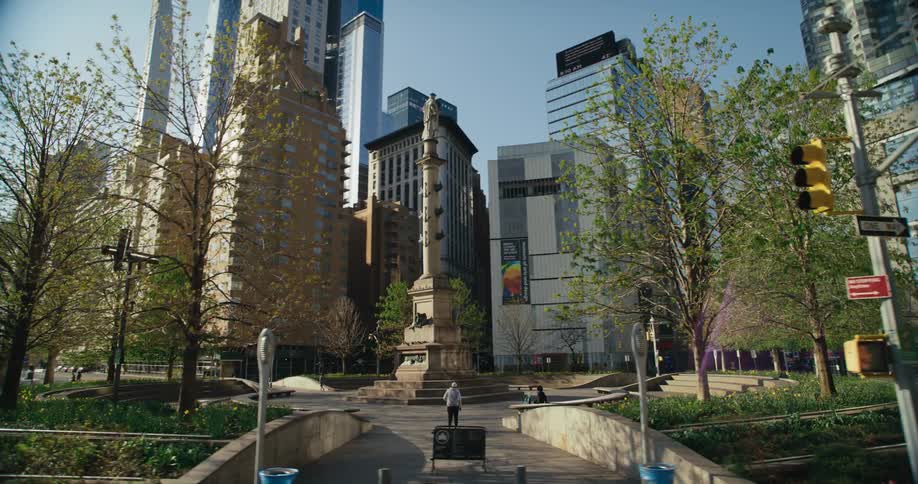 A person is walking through a downtown park surrounded by tall buildings on the street