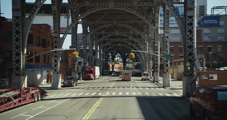 An ambulance with its lights flashing waits at an intersection below a bridge downtown