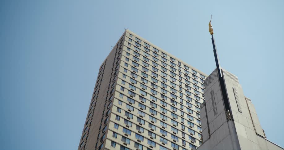 An angel moroni statue is on the steeple of a building in a city on a sunny day