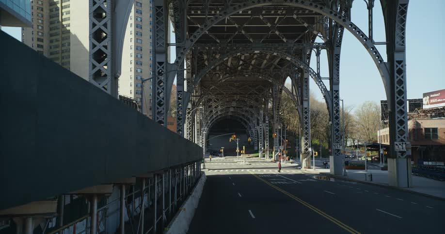 A person walks across the empty city street under the elevated train platform