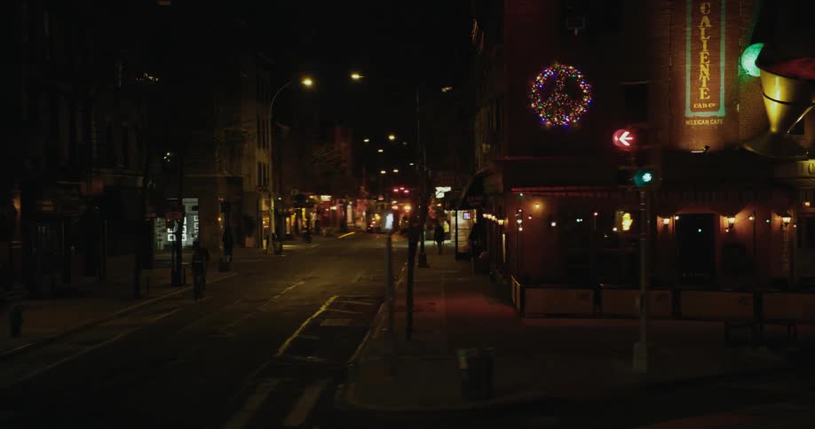 People walk down the center of the road in a city lit up at night