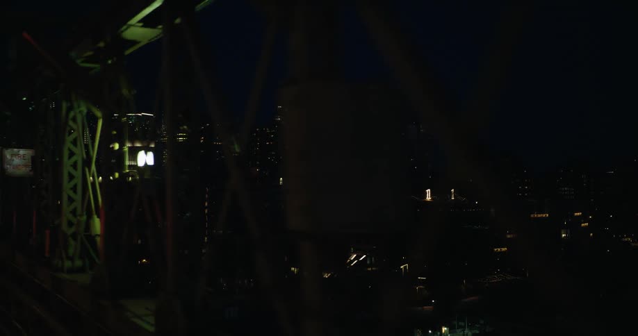 Lit welcome sign shining from on top of building is visible through bridge struts at night