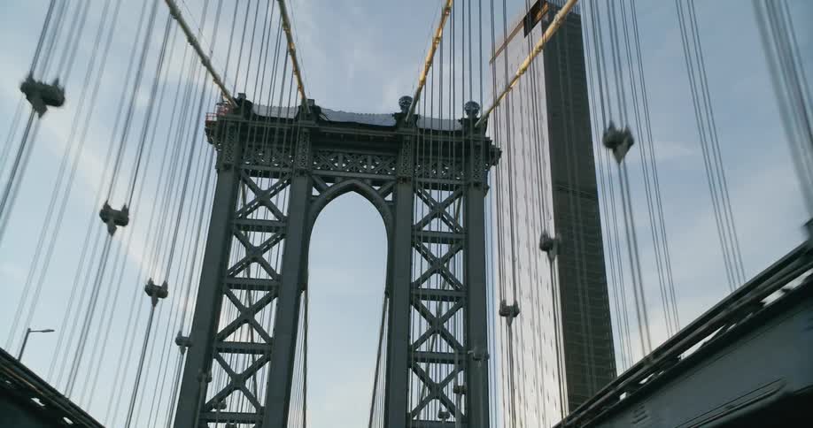 Vehicle crosses the bridge with tower and cables against the skyscraper
