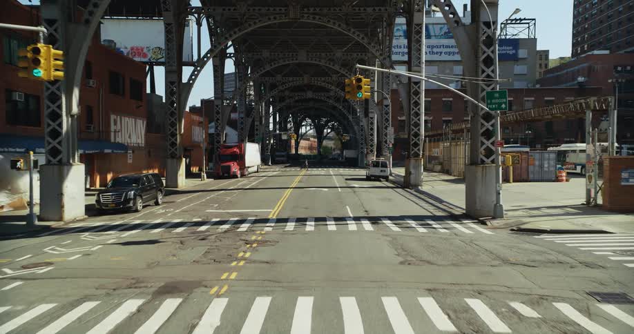 A person crosses the city street under the elevated train tracks pushing a carriage ahead